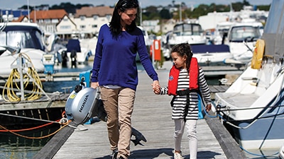A woman holding hands with her daughter carrying a Honda outboard